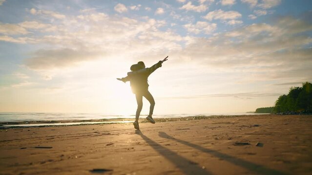 Happy woman skipping on sand sea beach. Female tourist rejoicing vacations walking along ocean jumping turning feeling freedom. Hiker carrying touristic backpack. Tourism travel wanderlust concept.