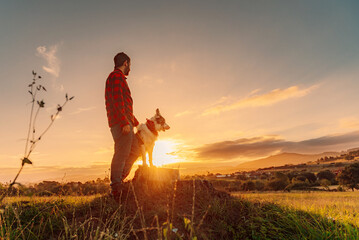 Young man standing in the field with his border collie dog watching the sunset.