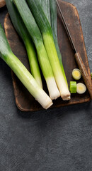 Cut fresh leeks on wooden board. Dark background.