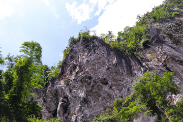 View from the bottom of the cliff. mountain peak and clear sky, green tree with white clouds....