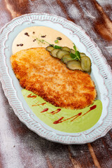 Viennese chicken schnitzel with sauces and pickles. Haute cuisine. On a wooden background.