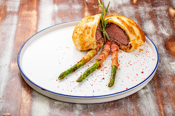 Wellington beef, with bacon-wrapped sprigs. Haute cuisine. On a wooden background.