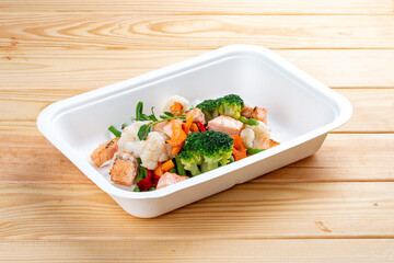 Baked salmon with vegetables. Healthy diet. Takeaway food. Eco packaging. On a wooden background.