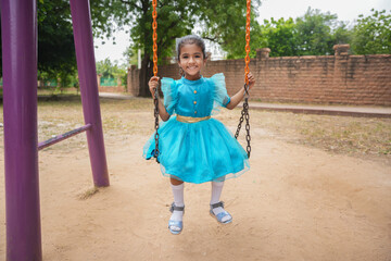 Happy little indian girl having fun on a swing on sunny day. Healthy summer activity for children.