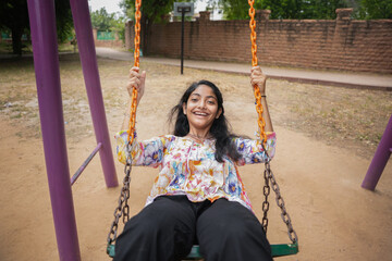 Happy indian girl having fun on a swing on sunny day. Healthy summer activity for children.