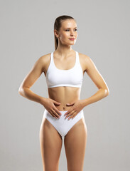 Fototapeta premium Young and beautiful slender girl in white swimsuit posing over white background. Healthcare, diet, sport and fitness concept.