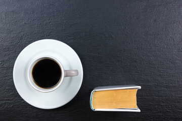 Cup of coffee and book on black wooden background. top view.