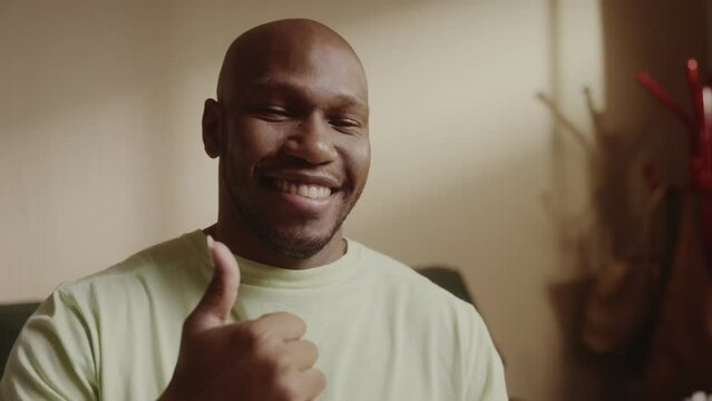 Homem negro sorridente sentado na cama fazendo sinal de postivo com os polegares. Cinematico 4k.