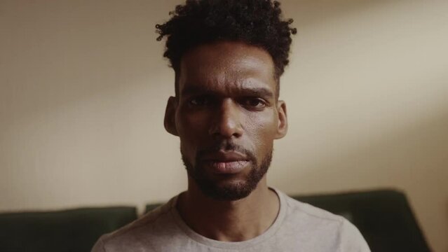 Homem negro sentado na cama com expressao seria. Cinematico 4k.