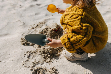 Child playing with sand, using a shovel, at the beach, closeup.