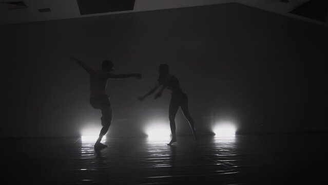 Modern ballet dancers performing together on dark stage. Silhouette performers with smoke in the air.