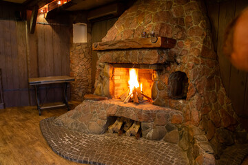 Old style stone fireplace. Wood burns in the fireplace with a blazing fire.