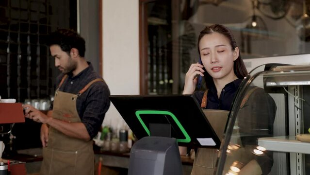 Two cheerful baristas running coffee shop using modern technology POS machine and laptop,  Indian worker making hot coffee by professional machine, Asian and Indian couple small business owner