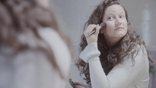 Mulher jovem aplicando blush com pincel de maquiagem no banheiro. Cinematico 4k.