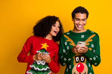 Photo of positive cute lady guy wear new year ugly print sweaters texting apple samsung iphone devices isolated yellow color background