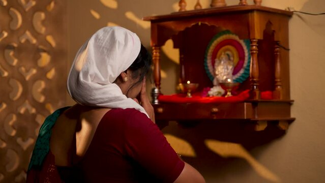 Shoulder shot of devotional Indian woman praying god after taking bath during early morning at home - concept of spirituality, Hinduism and traditional custom or rituals