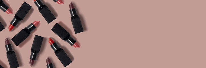 Different red colored lipsticks with black tube on the beige background. Empty space