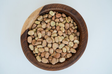 Dried fava beans on a wooden plate isolated on a white background