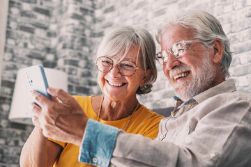 Happy retired family couple using mobile phone for video call together, talking to relations, getting good news, having fun, smiling and laughing. Carefree mature pensioners chatting online on cell.
