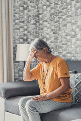 Sad depressed middle aged mature woman sitting alone at home touching head feeling headache migraine, upset tired old senior lady widow mourning suffer from grief loneliness mental problems concept. - obrazy, fototapety, plakaty