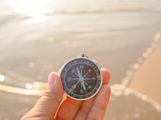 Close up hand holding compass with beach background