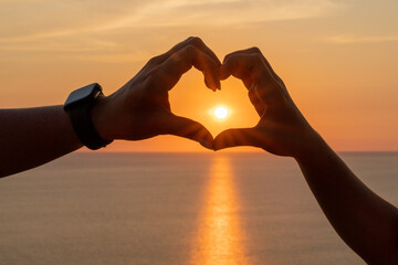 Hands heart sea sanset. The image features a beautiful sunset with two people holding their hands up in the air, forming a heart shape.