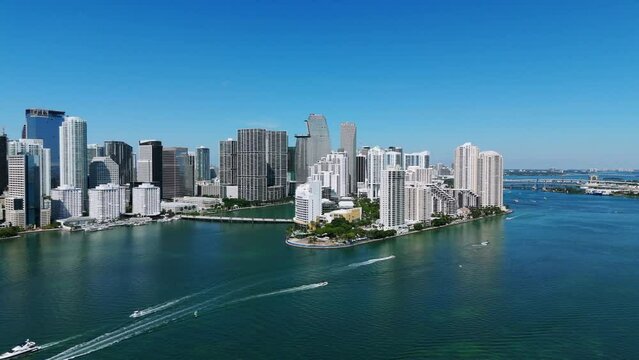 Sailboats crossing waters of blue ocean with Miami skyline in background. Drone view of thriving residential area with scyscrapers in Brickell Key, Miami downtown