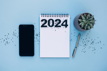 New year resolutions 2024 concept. 2024 goals list with notebook, pen, plant and phone on table. Resolutions, plan, goals, action, checklist, idea concept