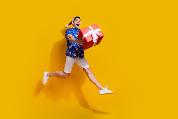 Obraz premium Full size photo of impressed energetic guy jump arms hold newyear giftbox empty space isolated on yellow color background