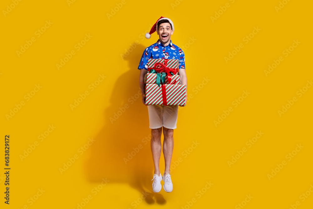 Poster Full size portrait of excited astonished guy jumping arms hold pile stack newyear giftbox isolated on yellow color background