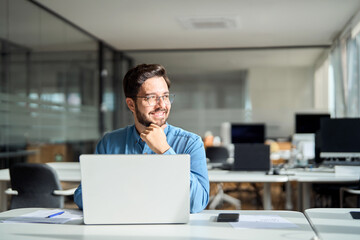 Happy smiling professional business man company employee, young male worker software developer, latin businessman working on laptop computer technology looking away at sunny office workplace desk. - obrazy, fototapety, plakaty