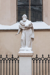 A snow-covered stone sculpture of a supposed Christian apostle holding a book stands outside the...