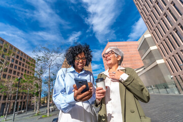 Fototapeta premium Multi-ethnic businesswomen laughing while using phone outdoors
