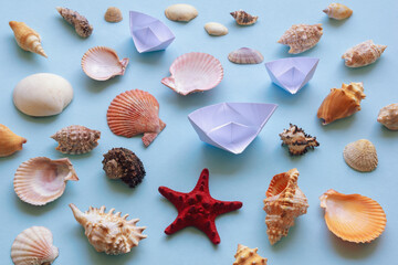 Different sea shells, starfish and white paper boats on blue background