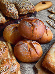 Close-up of freshly baked homemade wheat and rye rolls. In the background, various types of bread with sesame, sunflower and flaxseed seeds. Traditional bread from a Polish bakery.