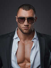 Handsome model in sunglasses and an open shirt, revealing his muscular torso, on a gray background