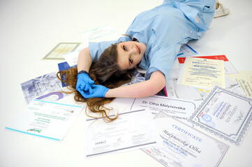 beautiful woman doctor in gloves and blue medical suit lies on diplomas certificates on the white floor medical education training courses doctor nurse dentist stomatology high qualification