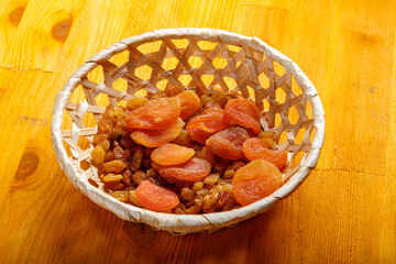 Dried apricots and raisins in a wicker plate on a wooden table.