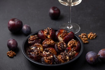 Plums baked with Camembert cheese, walnuts, honey and glass of white wine. Popular hot appetizer on a black plate. Selective focus, close-up.