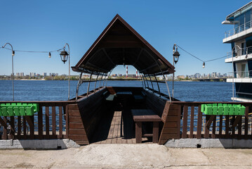 A wooden gazebo in the shape of a boat with a deck and a sail roof with lanterns and a garland of...