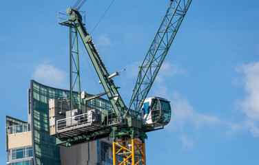 Tower cranes and unfinished buildings on background of blue sky with white clouds. Housing construction, apartment blocks in city.