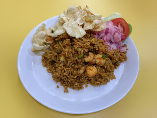 A typical aceh seafood fried rice called Nasi goreng seafood aceh, with lemon slices, tomatoes, cucumbers, shallots, shrimp, squid slices, chilies and Gnetum gnemon crackers