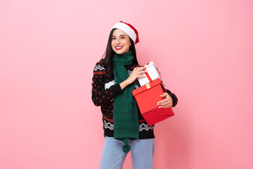 Festive portrait of beautiful woman wearing Christmas sweater and hat holding gift boxes in pink color isolated background studio shot