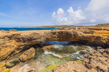 View of natural bridge on shores of Caribbean Sea in Aruba with caution signs indicating risk of bridge collapse.