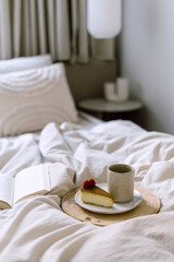 Wooden tray with cup of coffee and cheesecake on rumpled bedding in bedroom