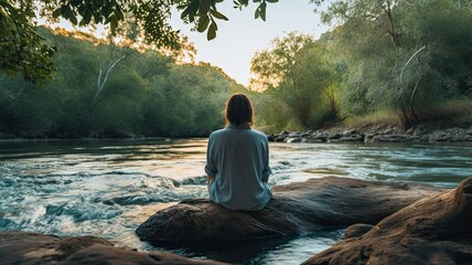 An image of a person sitting on a riverbank, with their feet dipped in the cool, flowing water, experiencing the soothing and meditative qualities of riverside serenity - obrazy, fototapety, plakaty