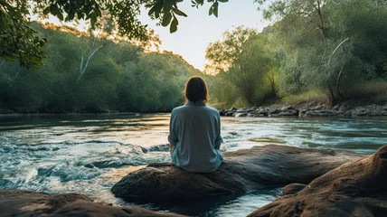 Foto op Canvas An image of a person sitting on a riverbank, with their feet dipped in the cool, flowing water, experiencing the soothing and meditative qualities of riverside serenity © kwanchaift