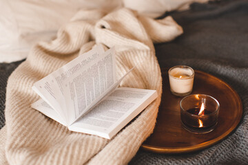 Scented burning candle with open paper book in bed close up. Aromatherapy.