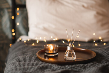 Home liquid fragrance in glass bottle with bamboo sticks and scented candle over glowing lights in bed close up. Aromatherapy. - Powered by Adobe