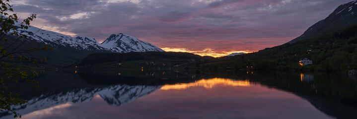 Stunning Norwegian lake scenery with snow covered mountains at dawn.	